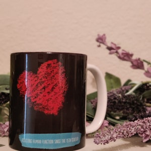 May include: A black ceramic mug with a red heart design and the text "Affecting human function since the 15th century".
