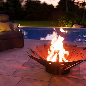 May include: A lit fire pit with a unique petal design sits on a patio near a pool. A chair, side table, and wine bottle are also visible. The scene is lit with warm, inviting light, suggesting an outdoor gathering.