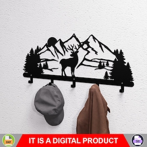 May include: Black metal wall-mounted coat rack featuring a mountain and deer silhouette design. The rack has three hooks and is decorated with trees and a sun. A gray cap and brown garment hang from the hooks. The text "IT IS A DIGITAL PRODUCT" is at the bottom.