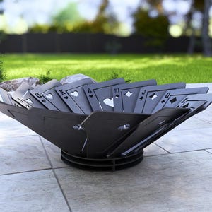 May include: A black metal fire pit with a unique design featuring playing card symbols. The fire pit is set on a tiled patio with a grassy background, perfect for outdoor gatherings.
