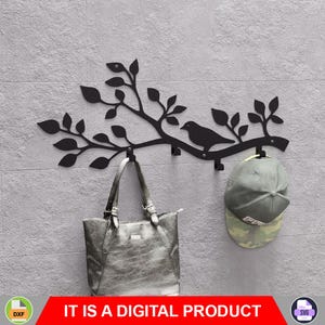 Puede incluir: Perchero de pared de metal negro con diseño de pájaro y rama. Un bolso tote de cuero gris y una gorra de béisbol de camuflaje cuelgan de los ganchos. El texto "IT IS A DIGITAL PRODUCT" se muestra en una pancarta roja.