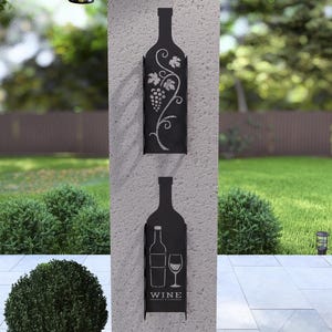 Puede incluir: Estante de pared para botellas de vino de metal negro con un dise&ntilde;o de vid y la palabra "WINE" en la parte inferior. El estante est&aacute; montado en una pared gris.