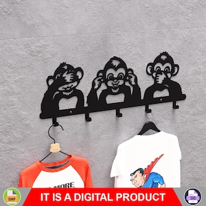 Puede incluir: Perchero de pared de metal negro con tres siluetas de monos en la pose "no ver el mal, no oír el mal, no hablar el mal". El perchero tiene tres ganchos y sostiene dos camisetas. El texto "IT IS A DIGITAL PRODUCT" está en la parte inferior.