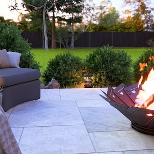 May include: A backyard patio scene featuring a modern fire pit with playing card cutouts, flames, and a gray lounge chair with pillows. A small table with a bottle of wine and a blanket complete the outdoor setting.
