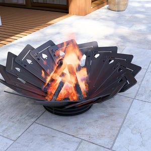 May include: A dark metal fire pit with a unique design featuring playing card symbols. The fire pit is filled with burning wood, producing bright orange flames. The fire pit is sitting on a light gray tiled surface.