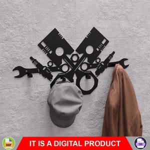 以下が含まれることがあります： 黒い金属製の壁掛けコートラック。エンジンピストン、レンチ、スパークプラグが交差しています。グレーのキャップがラックに掛けられ、右側には茶色のコートが掛けられています。「IT IS A DIGITAL PRODUCT」というテキストが下にあります。