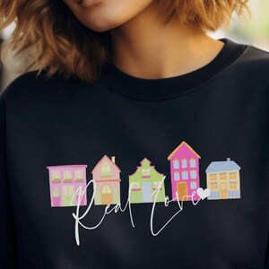 May include: Black sweatshirt with a graphic of colorful houses and the text "Real Love" in white script.