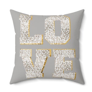 May include: A gray throw pillow with the word "LOVE" spelled out in gold letters. The letters are filled with white pearl-like beads.