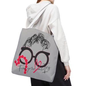 以下が含まれることがあります： グレーのトートバッグに、眼鏡をかけた人の白黒のイラストが描かれています。眼鏡には赤いハートが描かれており、左側に赤いビーズの紐が付いています。イラストの下には「Find your inner Tris」という文字が書かれています。