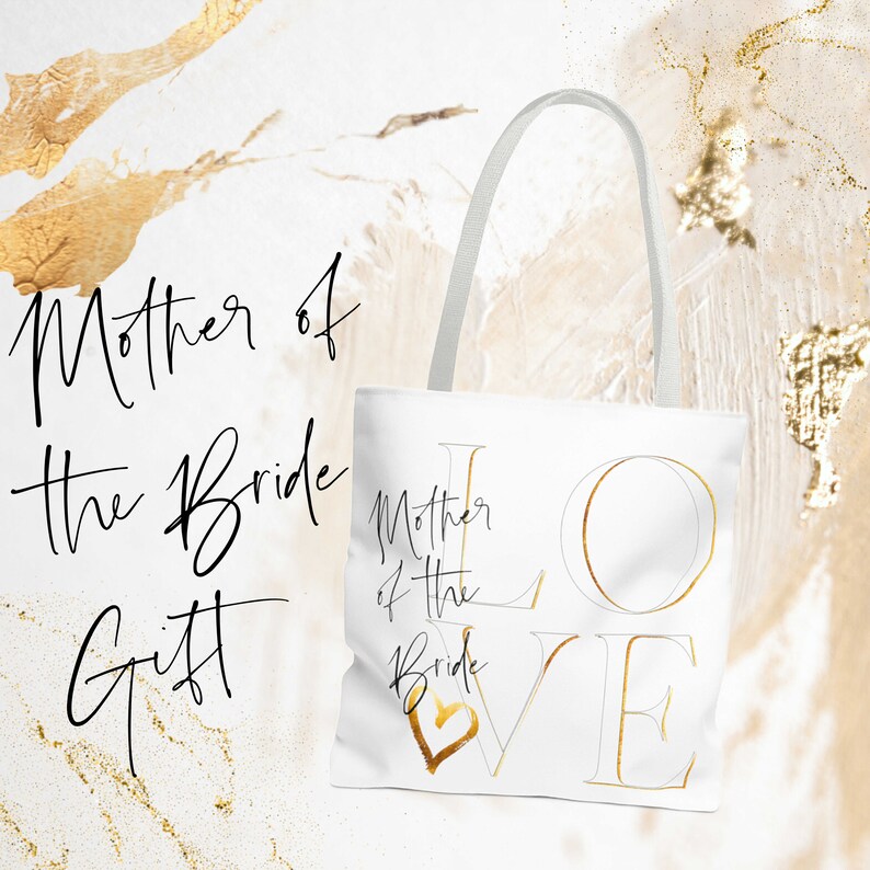 Puede incluir: Bolsa de tela blanca con letras doradas que dicen "Mother of the Bride" y "LOVE" con un coraz&oacute;n dorado en la esquina.