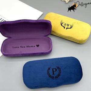 Może przedstawiać: Trzy aksamitne etui na okulary w różnych kolorach. Fioletowe etui ma napis "Love You Mama" z symbolem serca. Żółte etui ma wzór jelenich rogów z literami "AW" w środku. Niebieskie etui ma literę "P" w wieńcu.