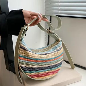 May include: A half-moon shaped handbag with a colorful striped pattern. The bag features a woven design with horizontal stripes in shades of blue, orange, red, and beige. It has a light green strap and gold-colored hardware.