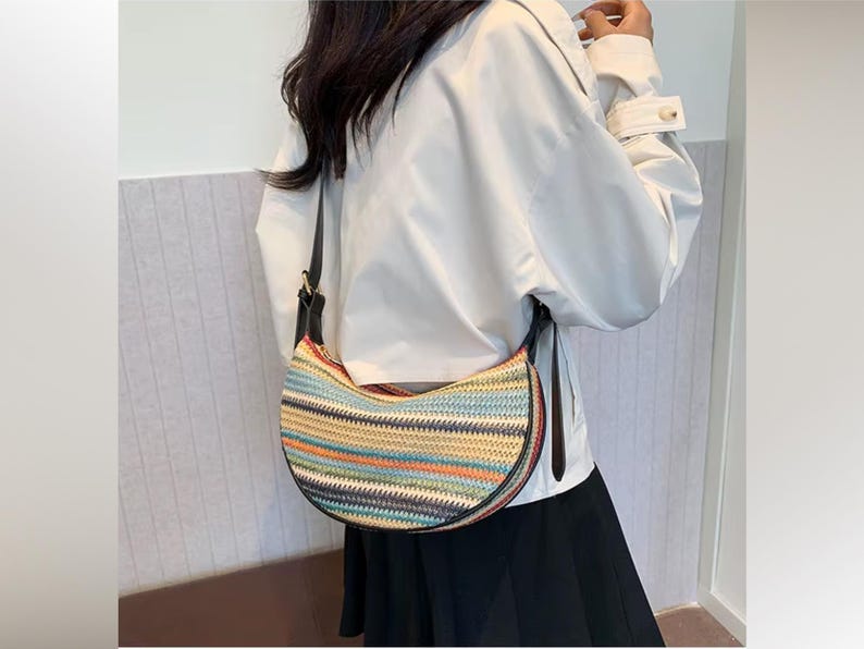 May include: A half-moon shaped handbag with a woven design in various colors, including blue, orange, and green. The bag has a black strap and trim. The bag is worn over the shoulder.
