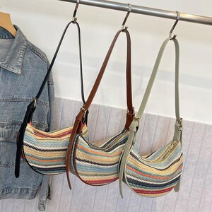 May include: Three shoulder bags with striped patterns in various colors, including blue, red, and yellow, hang from a metal bar. Each bag has a different strap color: black, brown, and light green. A denim jacket hangs on a wooden hanger to the left.