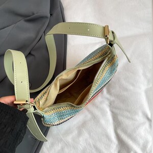 May include: A woven shoulder bag with a light green strap and gold-colored hardware. The bag features a colorful pattern of blue, yellow, and red. The interior of the bag is visible, showing multiple compartments.