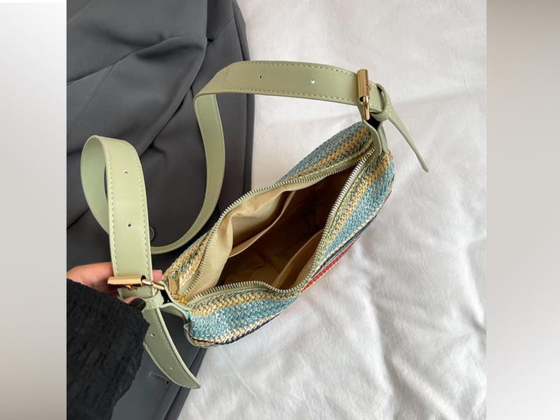 May include: A woven shoulder bag with a light green strap and gold-colored hardware. The bag features a colorful pattern of blue, yellow, and red. The interior of the bag is visible, showing multiple compartments.