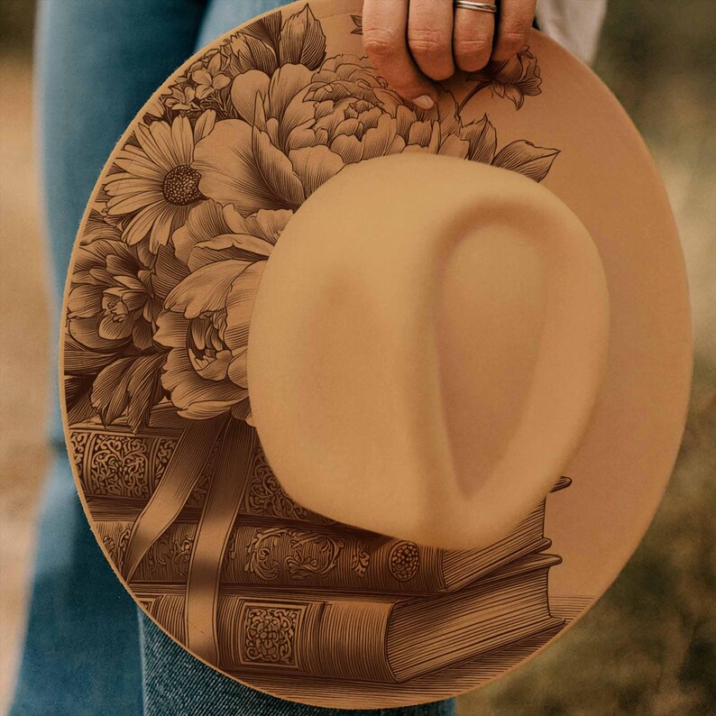 K&ouml;nnte beinhalten: Ein beigefarbener Fedora-Hut mit einem detaillierten Blumen- und Buchdesign. Der Hut hat eine breite Krempe und eine abgerundete Krone. Das florale Design umfasst Pfingstrosen und G&auml;nsebl&uuml;mchen. Die B&uuml;cher sind mit dekorativem Band gestapelt.