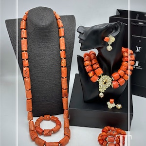 Op de afbeelding: Een koraalkleurige sieradenset tentoongesteld op zwarte mannequins. De set bevat een lange ketting, een armband, een ketting met meerdere strengen, oorbellen, een ring en een armband. De sieraden hebben rechthoekige kralen en gouden accenten. De merknaam "TOPHER TONY" is zichtbaar.