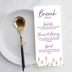 May include: A white plate with a gold and black fork tied with twine, next to a vertical menu card titled Brunch menu. The menu lists Salads, Bread & Bakery, and Sweet items in purple text, decorated with a row of light pink tulips at the bottom.