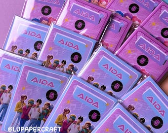 May include: A collection of mini coloring books with a purple and blue color scheme. Each book features the word "AIDA" and the number "5". The books have illustrations of a group of people and musical notes. The text "K-POP DEMONS MINI COLORING BOOK" is at the bottom.