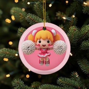 May include: A round, pink Christmas ornament featuring a cartoon cheerleader with blonde hair, a pink uniform, and white pom-poms. The ornament is hanging from a gold string against a backdrop of a Christmas tree.