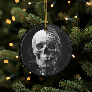 May include: A round, black and white Christmas ornament featuring a detailed illustration of a skull. One half of the skull is a realistic human skull, and the other half is a mechanical representation. The ornament hangs from a gold string.