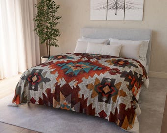 May include: A colorful patterned blanket with a geometric design in shades of red, orange, teal, and gray. The blanket is draped over a bed with white bedding. A decorative piece of art hangs on the wall above the bed.