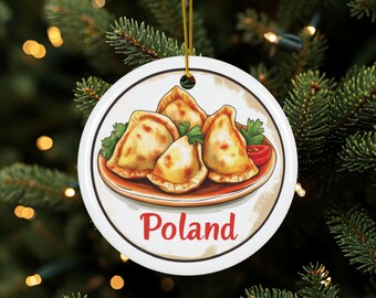 May include: A white ceramic Christmas ornament depicting a plate of pierogi, parsley, and a tomato slice. The word "Poland" is written in red script below the plate. The ornament hangs from a gold string.