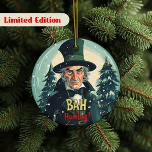 May include: A round Christmas ornament featuring a stern-looking man in a top hat and the words "BAH Humbug!". The ornament has a snowy background with Christmas trees and the text "Limited Edition". It is hanging from a gold string.