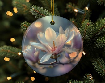 Może przedstawiać: Okrągła ozdoba choinkowa z bliskim ujęciem kwiatu magnolii. Kwiat ma białe płatki z różowym środkiem na rozmytym tle. Ozdoba zawieszona jest na złotym sznurku.