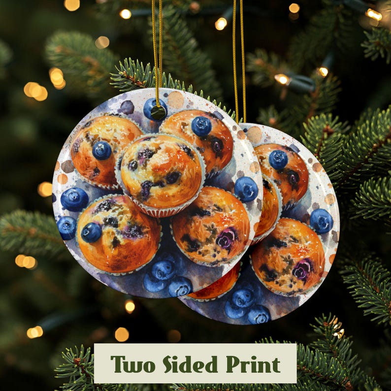 Baking blueberry muffins round ceramic ornament featuring a detailed image of freshly baked blueberry muffins with golden tops and scattered berries. The glossy finish enhances the warm tones of the muffins. High quality ceramic ornament hanging by a gold string. Pine tree in the background with lights behind the ornament. Showing the front and the back have the same print.