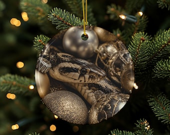 May include: Round Christmas ornament featuring a snake among gold and silver holiday decorations. The ornament has a gold string for hanging and is set against a backdrop of a Christmas tree with lights.
