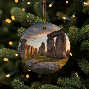Può includere: Ornamento natalizio rotondo con una vista panoramica di Stonehenge al tramonto. L'immagine mostra l'antico cerchio di pietra con un cielo dorato e erba verde. L'ornamento ha un cordino dorato per appenderlo.