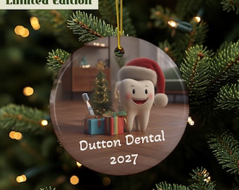 May include: A round Christmas ornament featuring a cartoon tooth wearing a Santa hat. The ornament includes a small Christmas tree, gifts, and the text "Dutton Dental 2027". The ornament is hanging from a gold string.