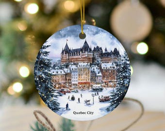 May include: A round ceramic ornament featuring a winter scene of the Chateau Frontenac in Quebec City, Canada. The ornament is white with a blue sky and snow-covered buildings. The text "Quebec City" is printed on the bottom of the ornament.