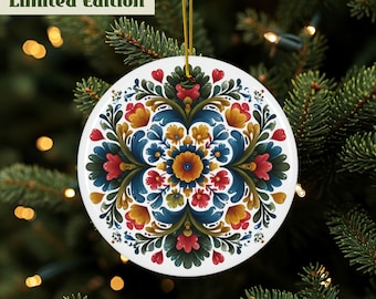 Op de afbeelding: Een witte, ronde kerstbal met een bloemenontwerp in rood, blauw, geel en groen. De ornament is opgehangen aan een gouden draad tegen een achtergrond van een kerstboom. De tekst "Limited Edition" staat bovenaan.