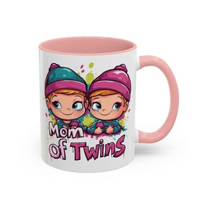 May include: White ceramic mug with a pink interior and handle. The mug features a cartoon illustration of two babies wearing hats, with the text "Mom of Twins" in pink and purple.