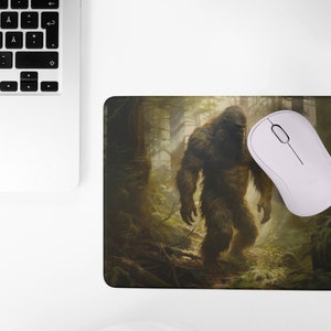 May include: A mouse pad with a brown and green forest scene featuring a large, hairy Bigfoot creature walking through the trees.