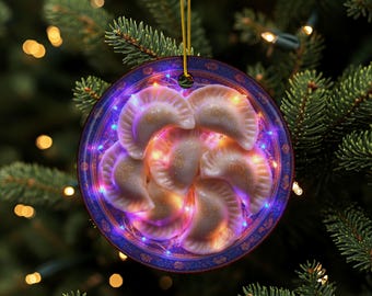 May include: A round Christmas ornament featuring a plate of pierogies, with a blue and purple border. The pierogies are illuminated with warm lights, and the ornament hangs from a gold string against a backdrop of a Christmas tree.