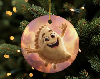 Puede incluir: Adorno navideño redondo con un personaje de pierogi de dibujos animados con una cara sonriente y los brazos extendidos. El adorno tiene una cuerda dorada para colgar y está sobre un fondo de puesta de sol. El adorno está colgado en un árbol de Navidad.