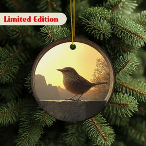 Könnte beinhalten: Runder Weihnachtsschmuck mit einer detaillierten Illustration eines kleinen braunen Vogels, der auf einer Steinmauer sitzt, vor einem warmen Sonnenuntergang. Der Schmuck hat einen Holzrahmen und eine goldene Aufhängeschnur. Der Text "Limited Edition" wird oben links angezeigt.