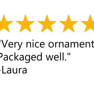 May include: Five gold stars above a customer review. The review reads: "Very nice ornament. Packaged well." Below the review is the name "-Laura".