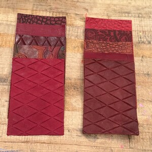 May include: Two stacks of red leather swatches with various textures and patterns. The swatches include diamond-stitched, embossed, and textured leather in shades of burgundy and crimson. The stacks are arranged vertically, showcasing the different designs.