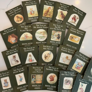 May include: A collection of Beatrix Potter books with green covers and illustrations. Titles include "The Tale of Peter Rabbit," "The Tale of Tom Kitten," and "The Tale of Squirrel Nutkin." The books are arranged on a white surface.
