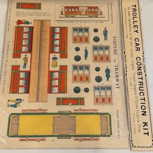 May include: A vintage trolley car construction kit with printed instructions and cut-out pieces. The kit includes illustrations of a trolley car, passengers, and the text "TROLLEY CAR CONSTRUCTION KIT". The kit is a reproduction of a French print.