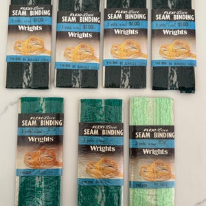 May include: An assortment of Flexi-Lace seam binding rolls in various shades of green. Each roll is labeled with the brand "Wrights" and includes the text "SEAM BINDING" and "3 yds."