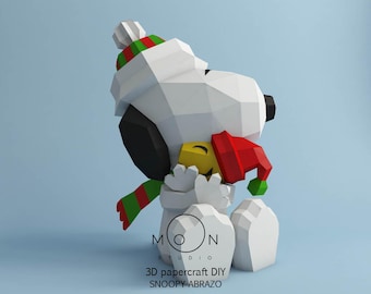 May include: A 3D papercraft Snoopy figure in a hugging pose, wearing a red and green hat and scarf. The figure is white with black ears and a yellow beak. The base of the figure has the text "MOON STUDIO" and "3D papercraft DIY SNOOPY ABRAZO".