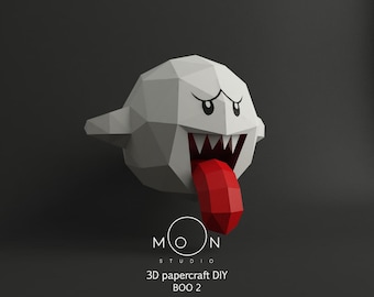 May include: A white papercraft model of a ghost with a red tongue and black eyes. The ghost is in a 3D pose with its mouth open and its tongue sticking out. The model is labeled "3D papercraft DIY BOO 2" and "MOON STUDIO".