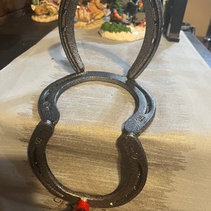 May include: Two silver horseshoes are stacked on top of each other to create a stocking holder. A red ribbon is attached to the bottom horseshoe.
