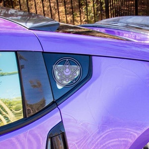 May include: A purple car with a black spoiler and white wheels. The car has a sticker on the back window with a pentagram design.